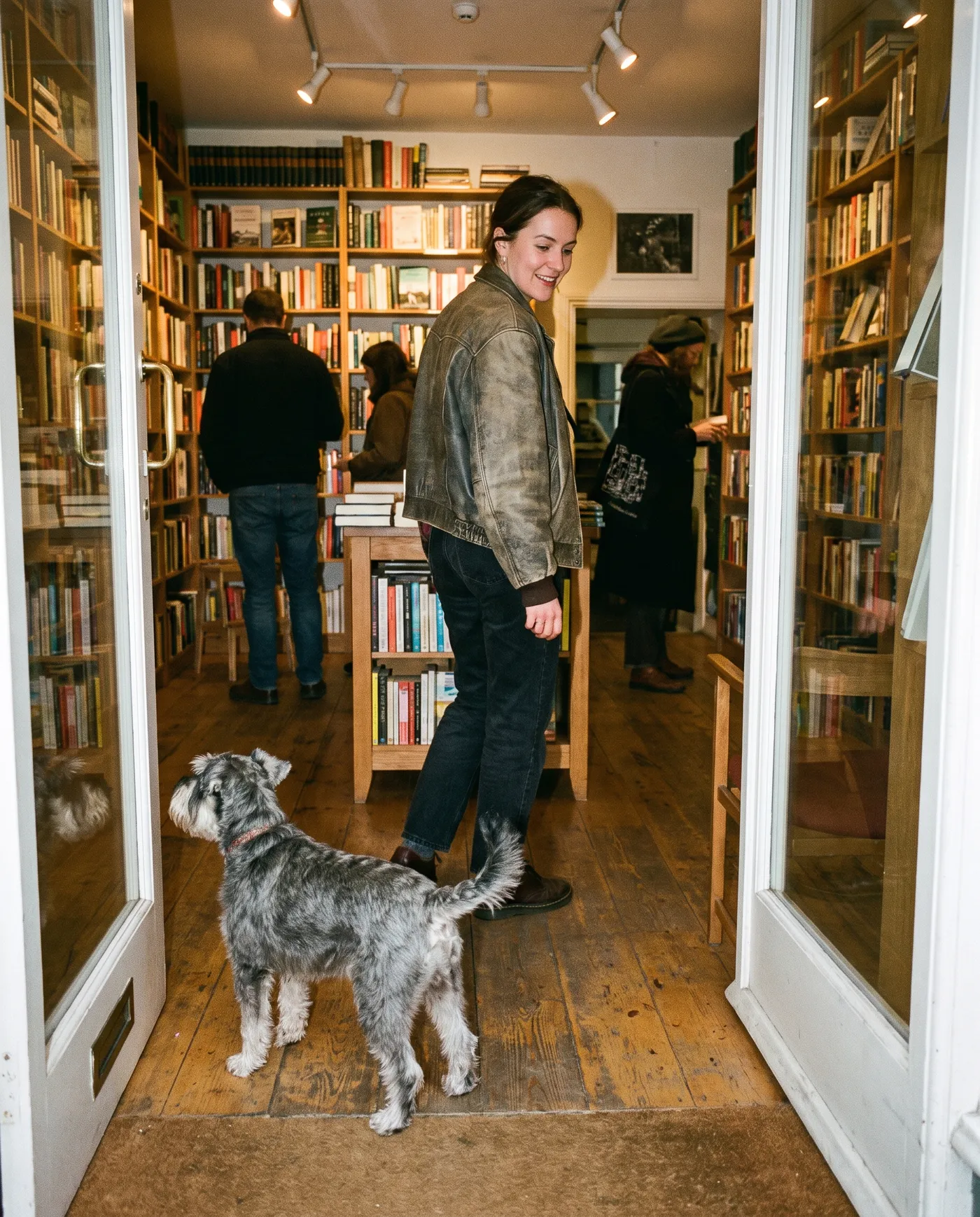 A woman stepping out of a bookshop doorway with a grey schnauzer walking ahead of her