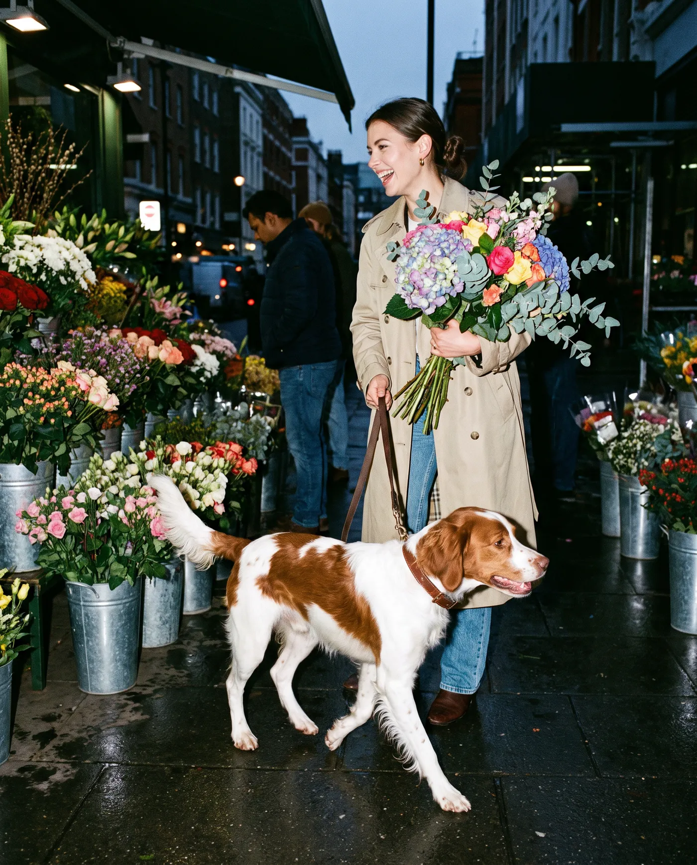 A woman carrying a large bouquet through a flower market with a brown and white spaniel on the lead